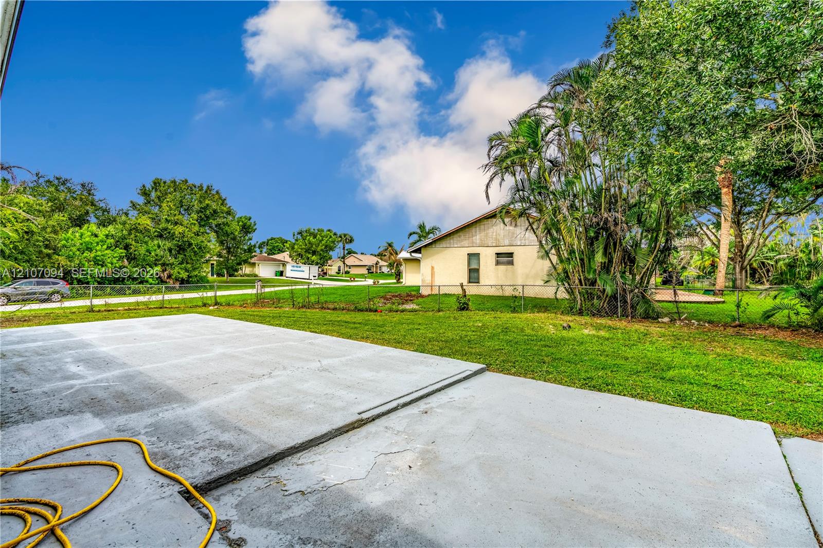 Spacious concrete patio overlooking a backyard featuring a grass lawn, mature palm trees, and metal perimeter fencing