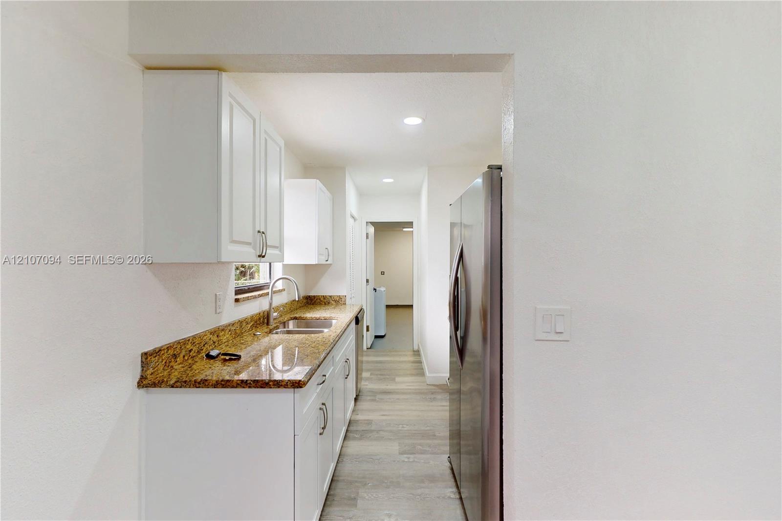 Kitchen featuring white shaker-style cabinetry, stone-finish countertops, stainless steel side-by-side refrigerator, dual-basin sink with arched faucet, and wood-finish flooring