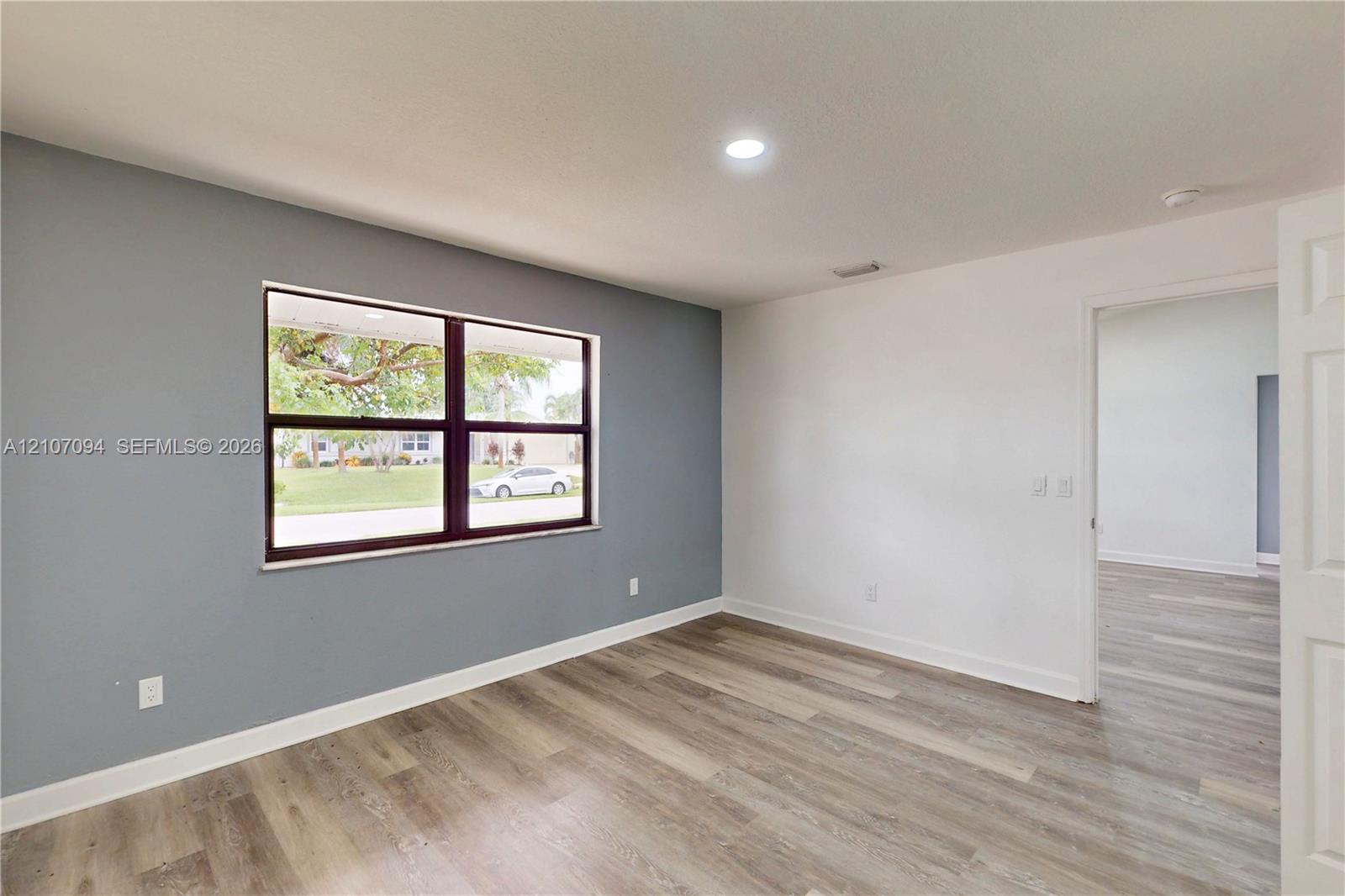 Neutral grey accent wall, expansive window, recessed lighting, and wood-finish flooring