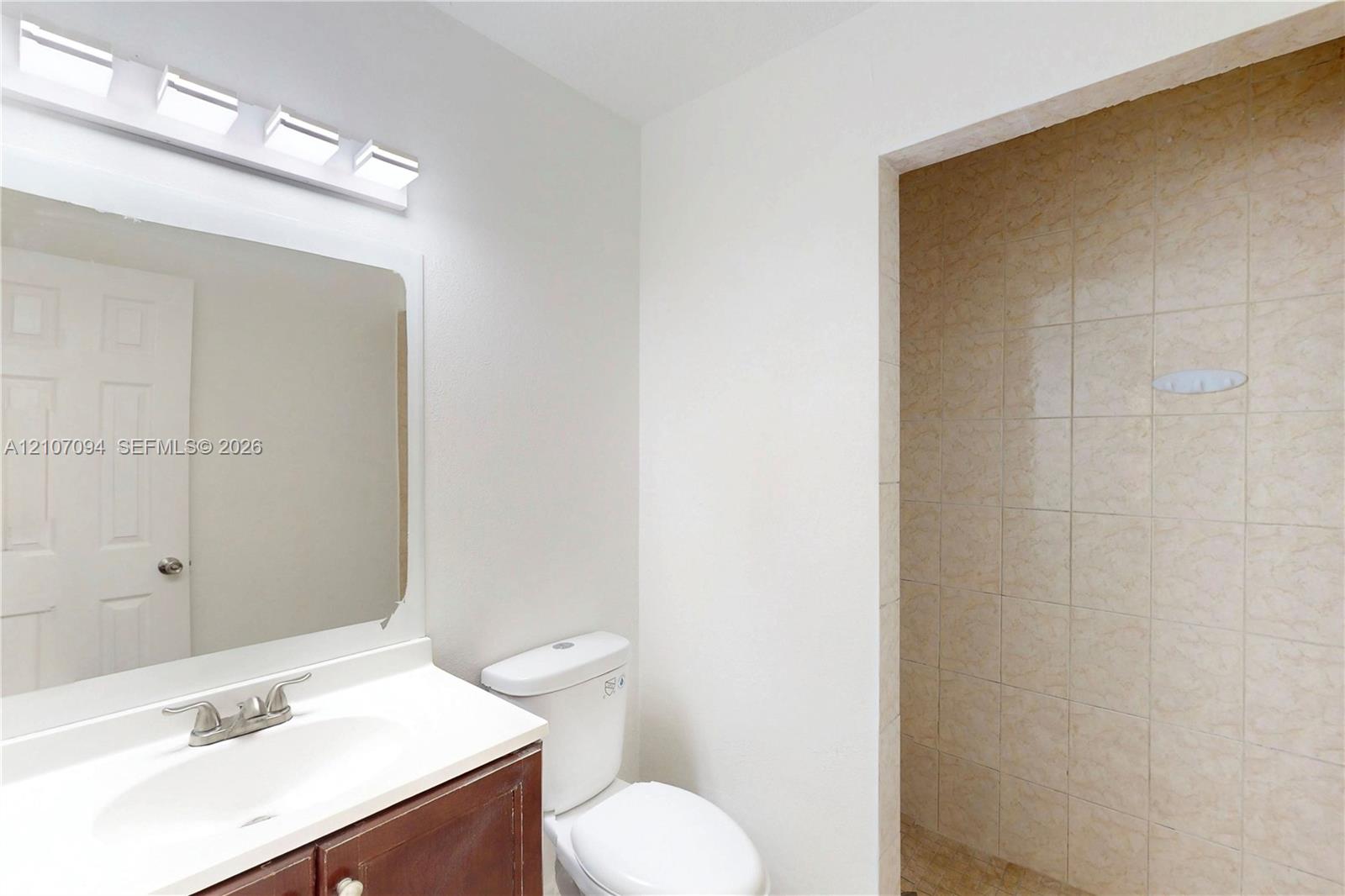 Bathroom featuring a vanity with an integrated sink, wall-mounted four-light fixture, framed mirror, and tiled shower enclosure
