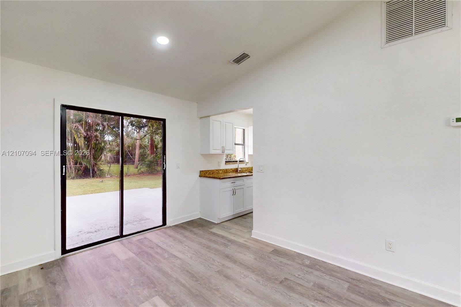 Vaulted ceiling, sliding glass doors, wood-finish flooring, and white cabinetry with stone-finish countertops