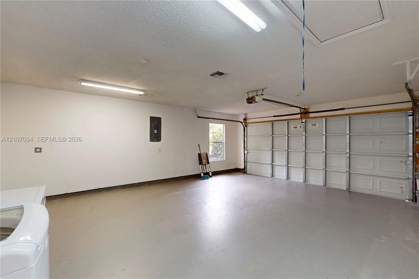 Multi-vehicle garage featuring a paneled sectional door, overhead fluorescent lighting, finished flooring, and an integrated electrical panel