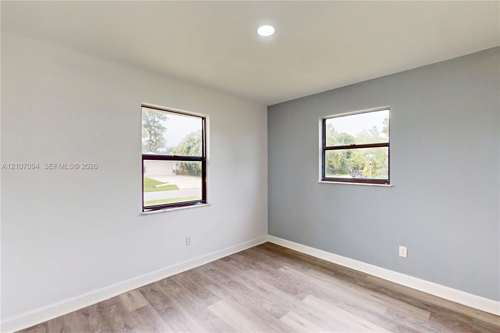 Room featuring wood-finish flooring, recessed lighting, and dual windows with dark frames, accented by a neutral-toned feature wall