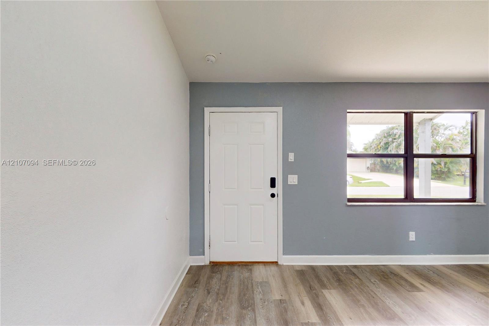 Entrance featuring a solid-panel door with integrated smart lock, wood-finish flooring, and large horizontal window with dark frame accents