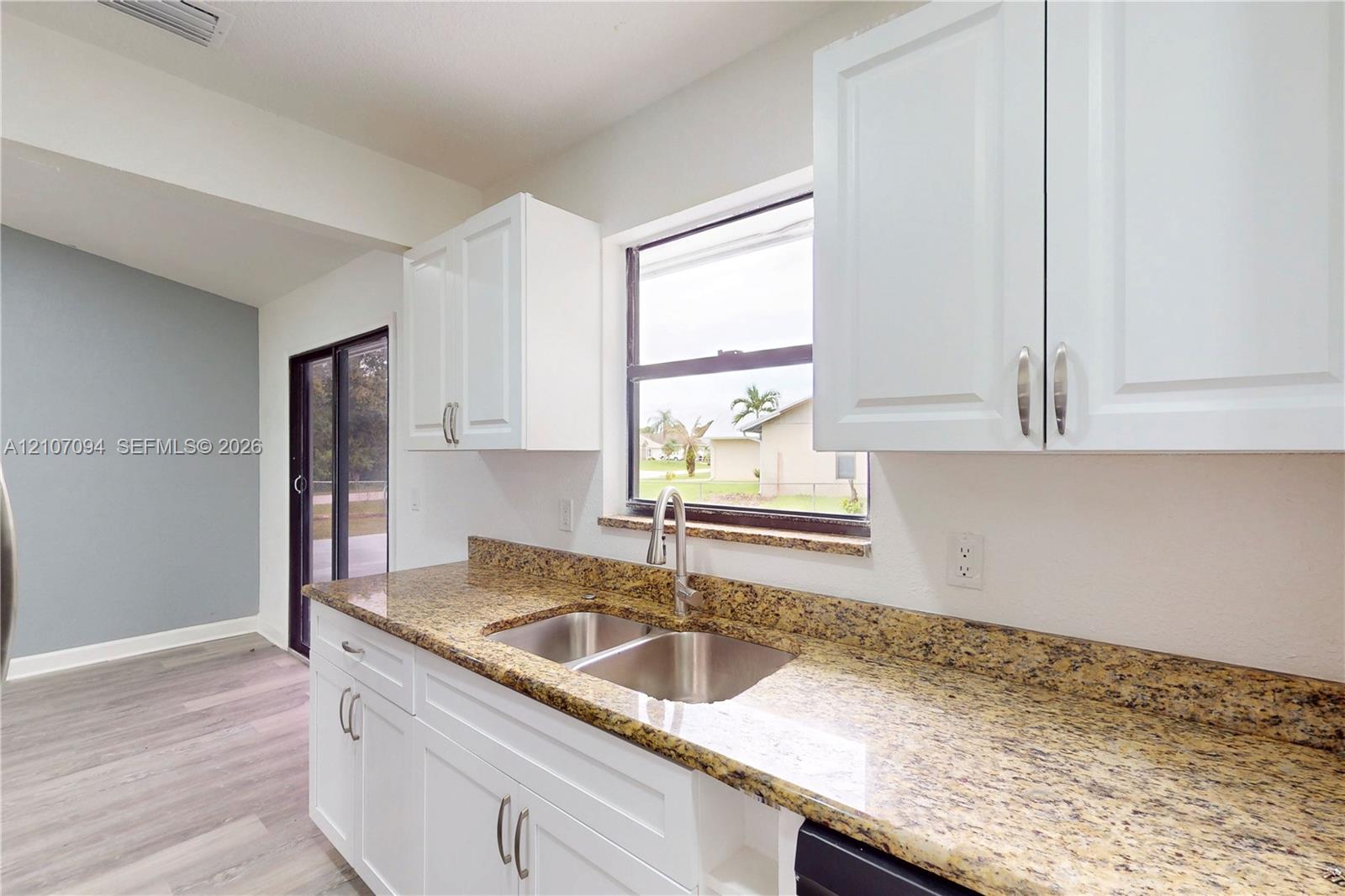 Kitchen featuring white Shaker-style cabinetry, stone-finish countertops, stainless steel dual-basin undermount sink with a gooseneck faucet, and wood-finish flooring