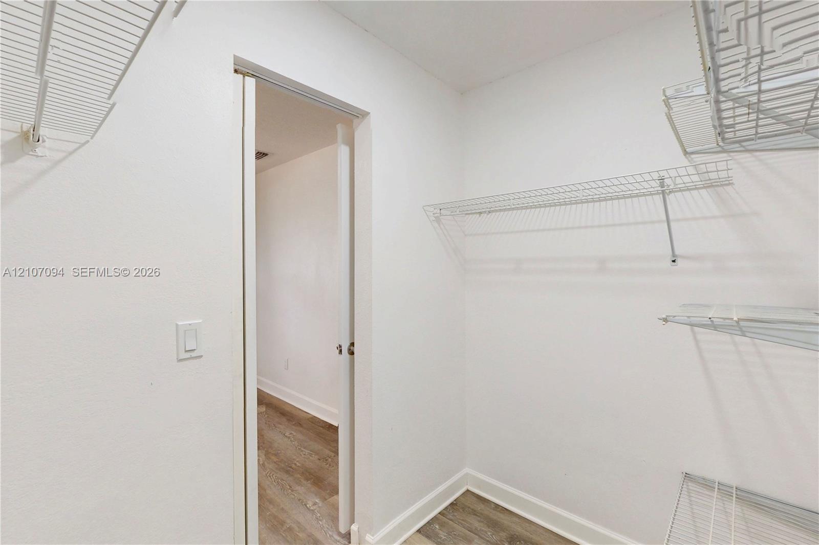 Storage area featuring white wall-mounted wire shelving and wood-finish flooring