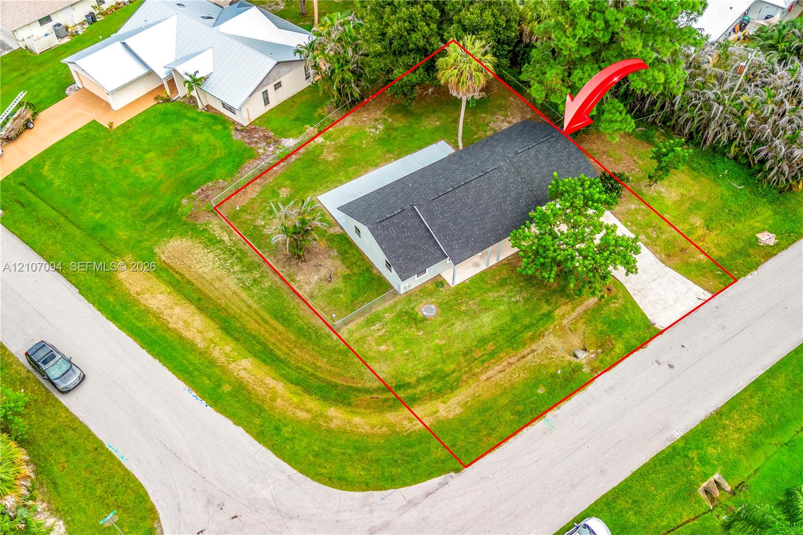 Aerial perspective of a corner lot property featuring a single-story residence with a shingled roof, concrete driveway, and expansive grass lawn