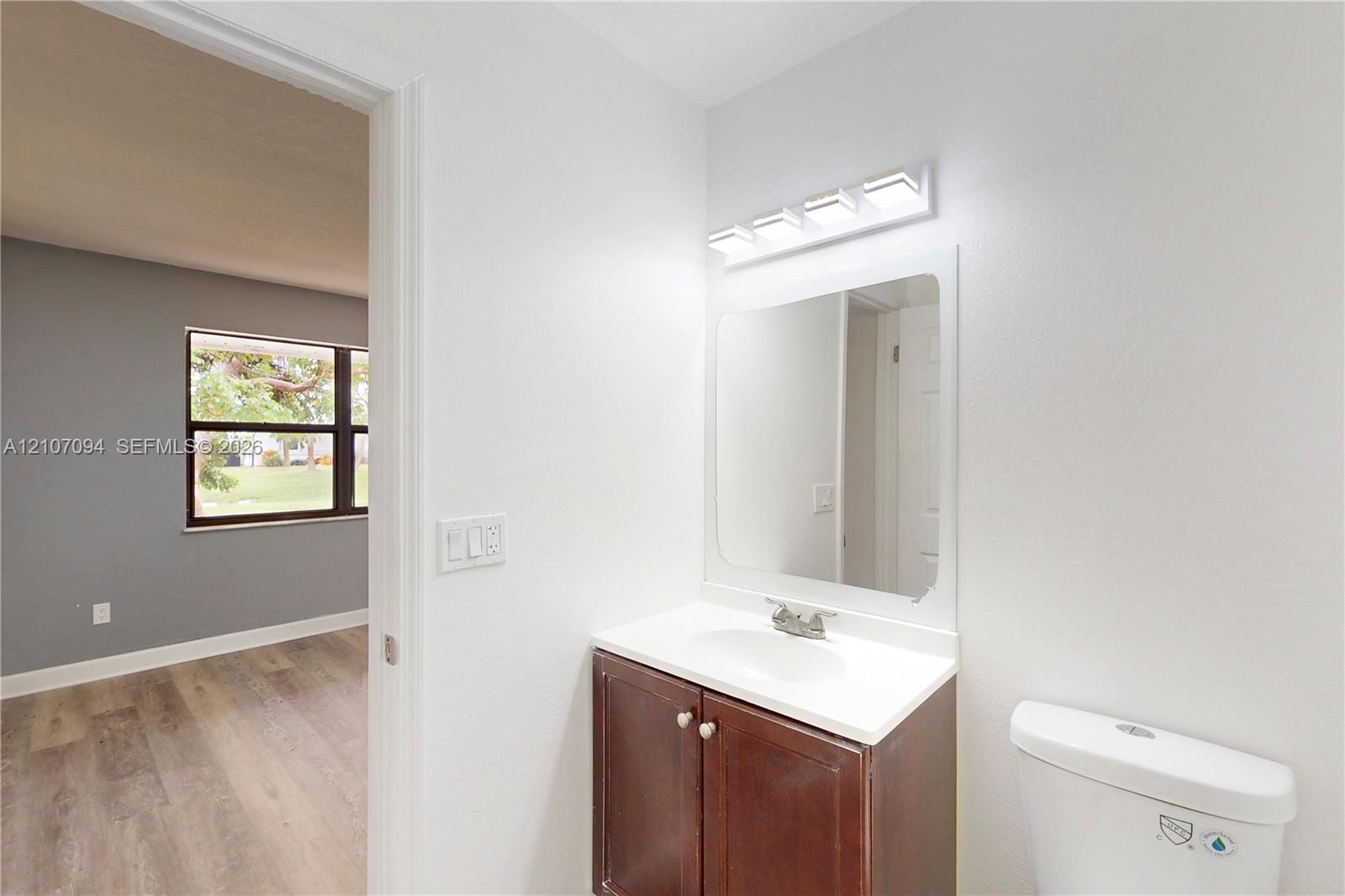 Vanity with integrated sink and countertop, polished chrome faucet, rectangular wall-mounted mirror, four-light vanity fixture, and wood-finish flooring
