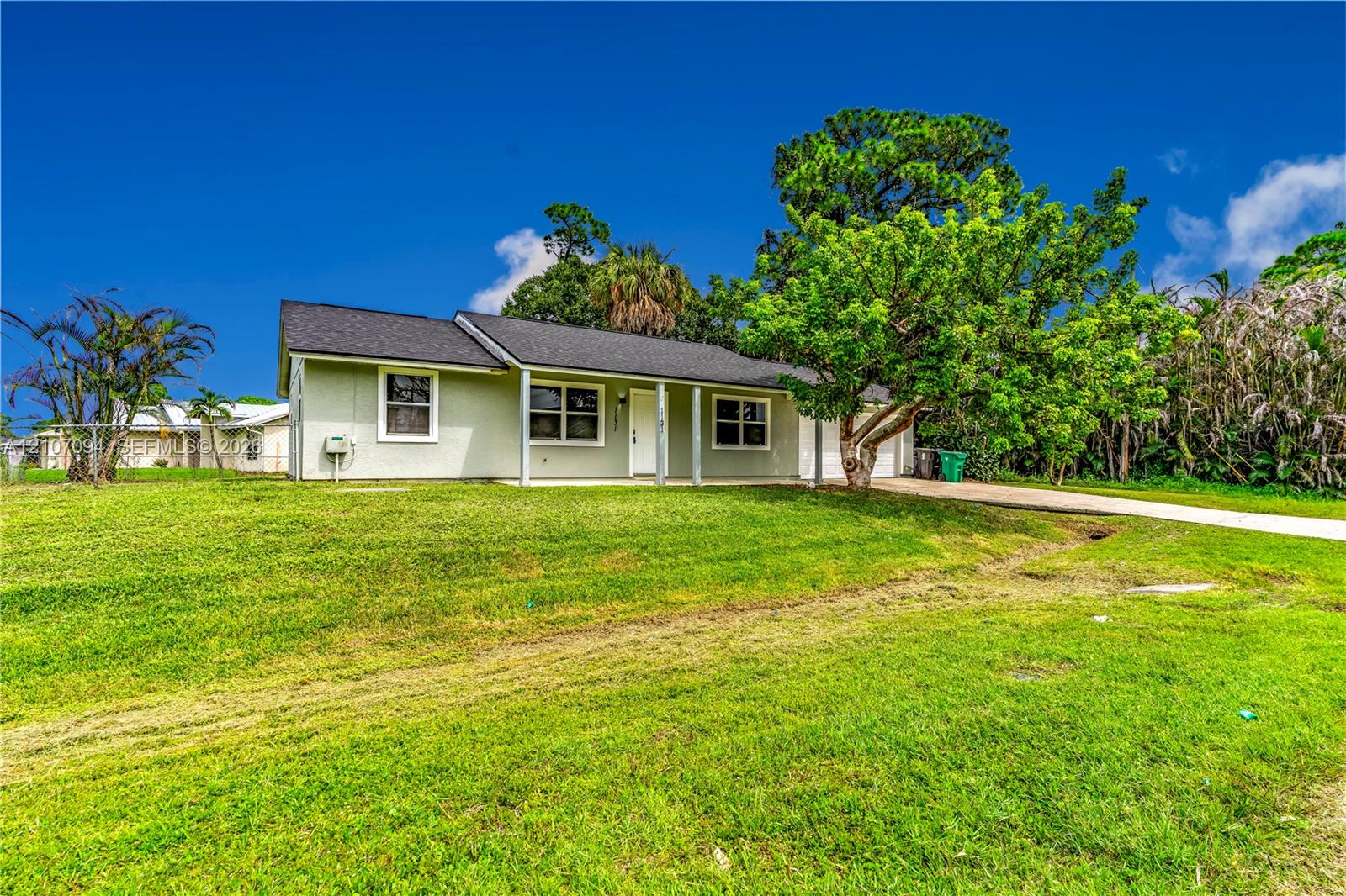 Single-story residence featuring a covered front porch, light-toned siding, dark shingled roof, and an expansive lawn