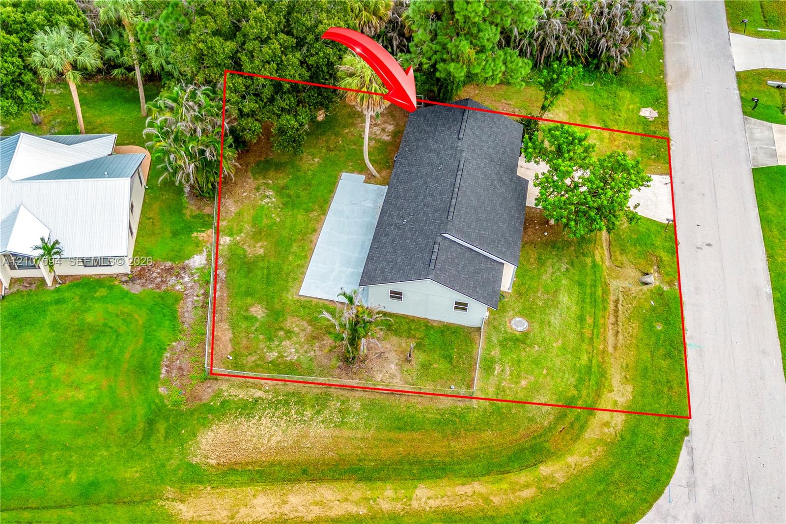 Aerial view of property featuring a detached residence with a composite shingle roof, concrete patio, concrete driveway, and mature landscaping on a grass-covered lot