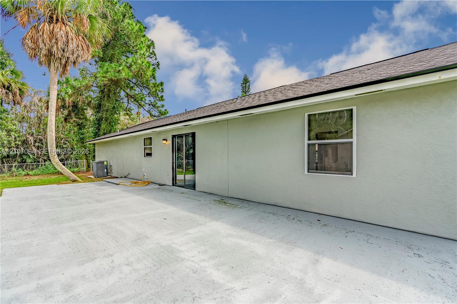 Rear exterior featuring a spacious concrete patio, stucco siding, sliding glass doors, and shingle roofing