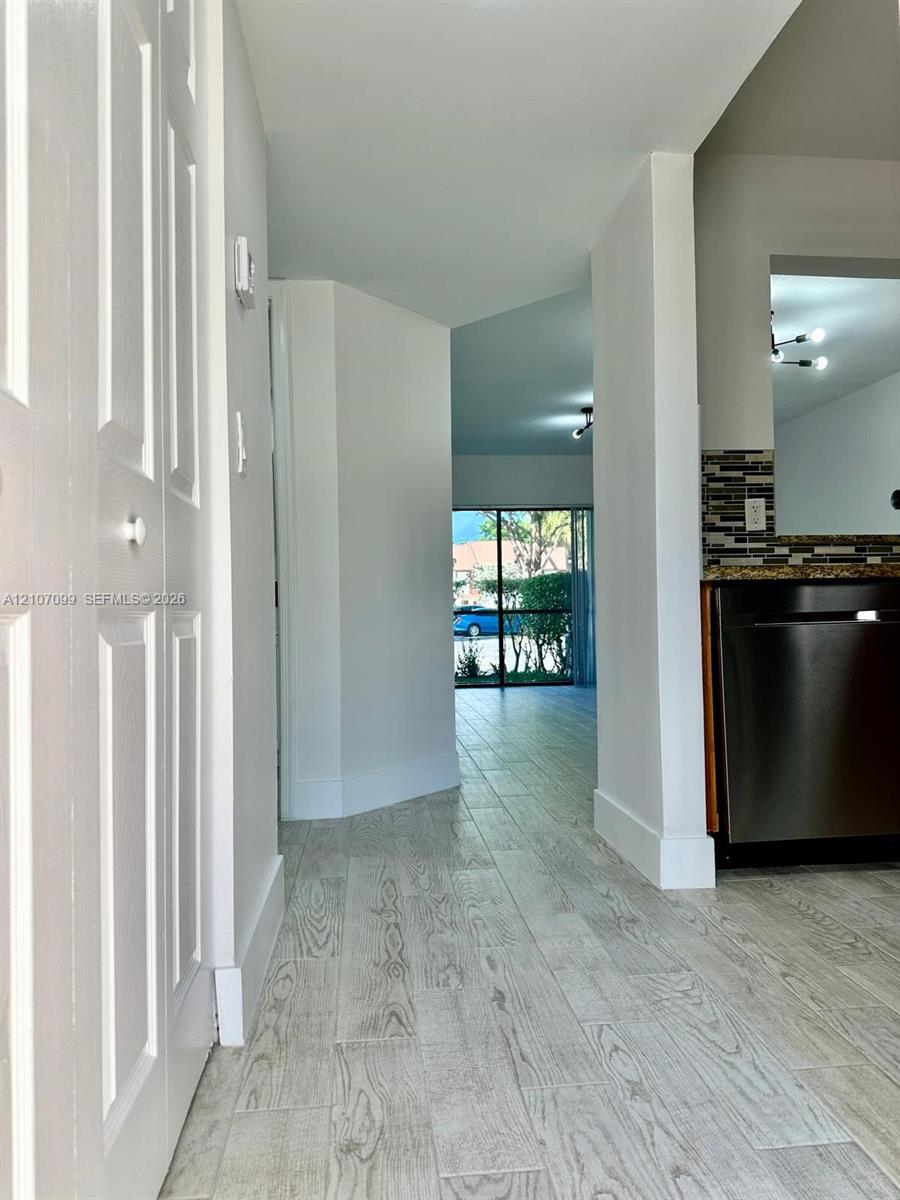Wood-finish flooring throughout, stainless steel dishwasher, mosaic tile backsplash, and floor-to-ceiling glass sliding door