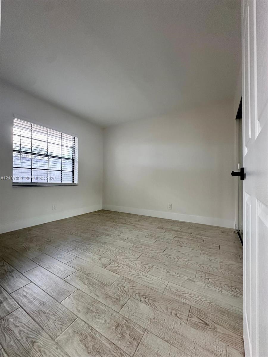 Room featuring wood-finish tile flooring, neutral wall paint, and a window with horizontal blinds