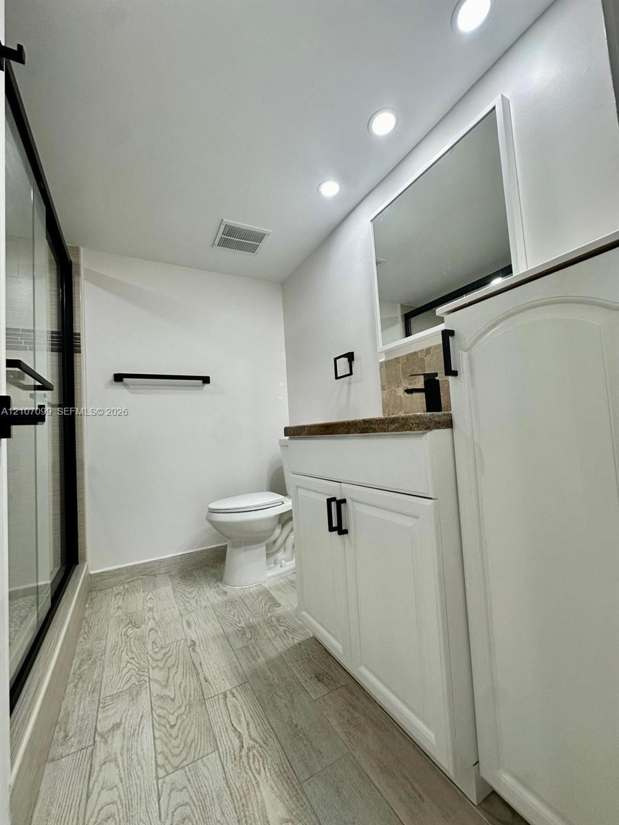 Bathroom featuring a vanity with stone-finish countertop, matte black hardware, recessed ceiling lighting, a walk-in shower with glass enclosure, and wood-finish flooring
