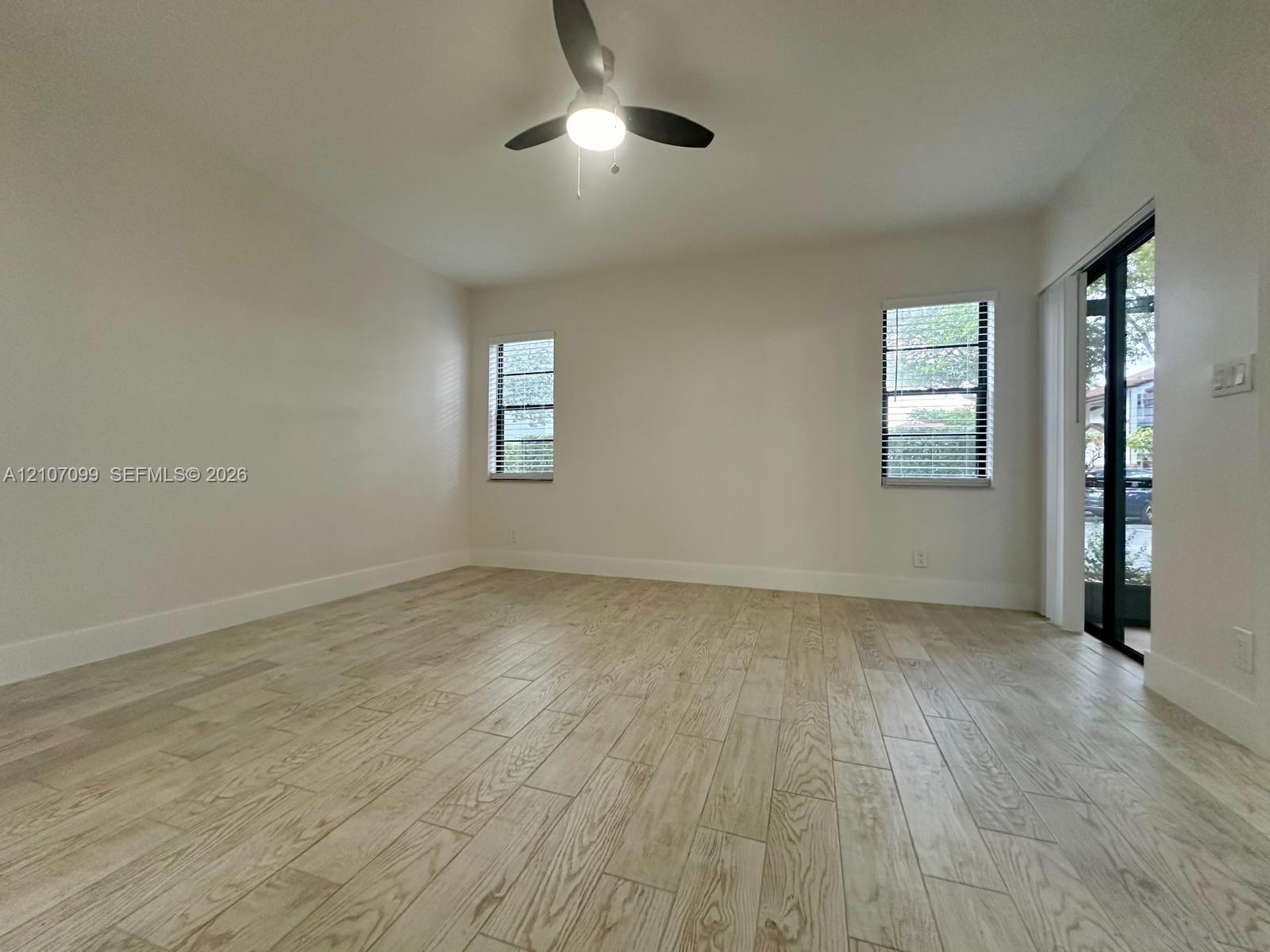 Neutral-toned wood-finish flooring, recessed lighting, ceiling fan with integrated light, multi-pane windows, and sliding glass door