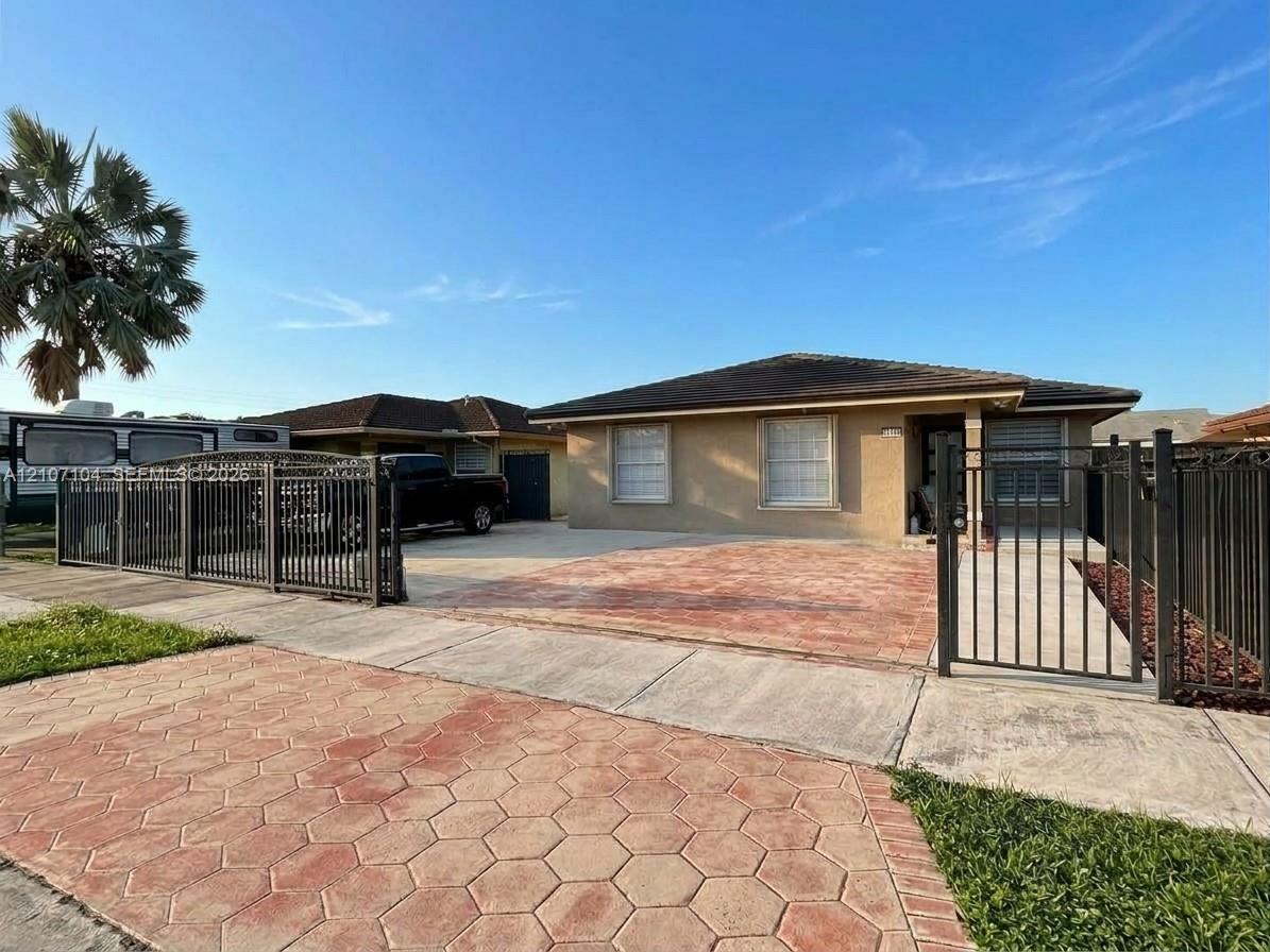 Single-story residence featuring a low-slope roof, stucco exterior, decorative hexagon-patterned paving, and perimeter metal fencing