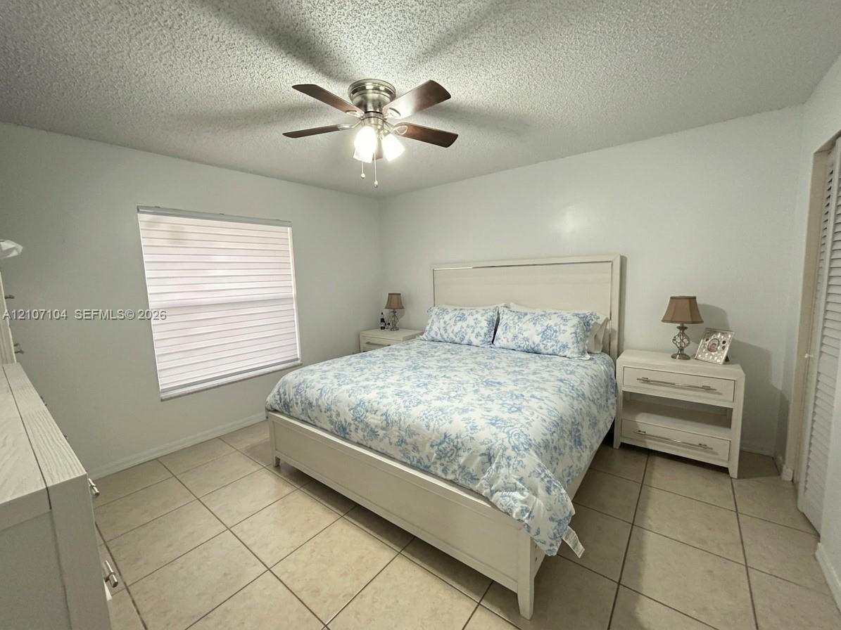 Neutral-toned ceramic tile flooring, ceiling fan with integrated light fixture, window with horizontal blinds, and louvered closet doors
