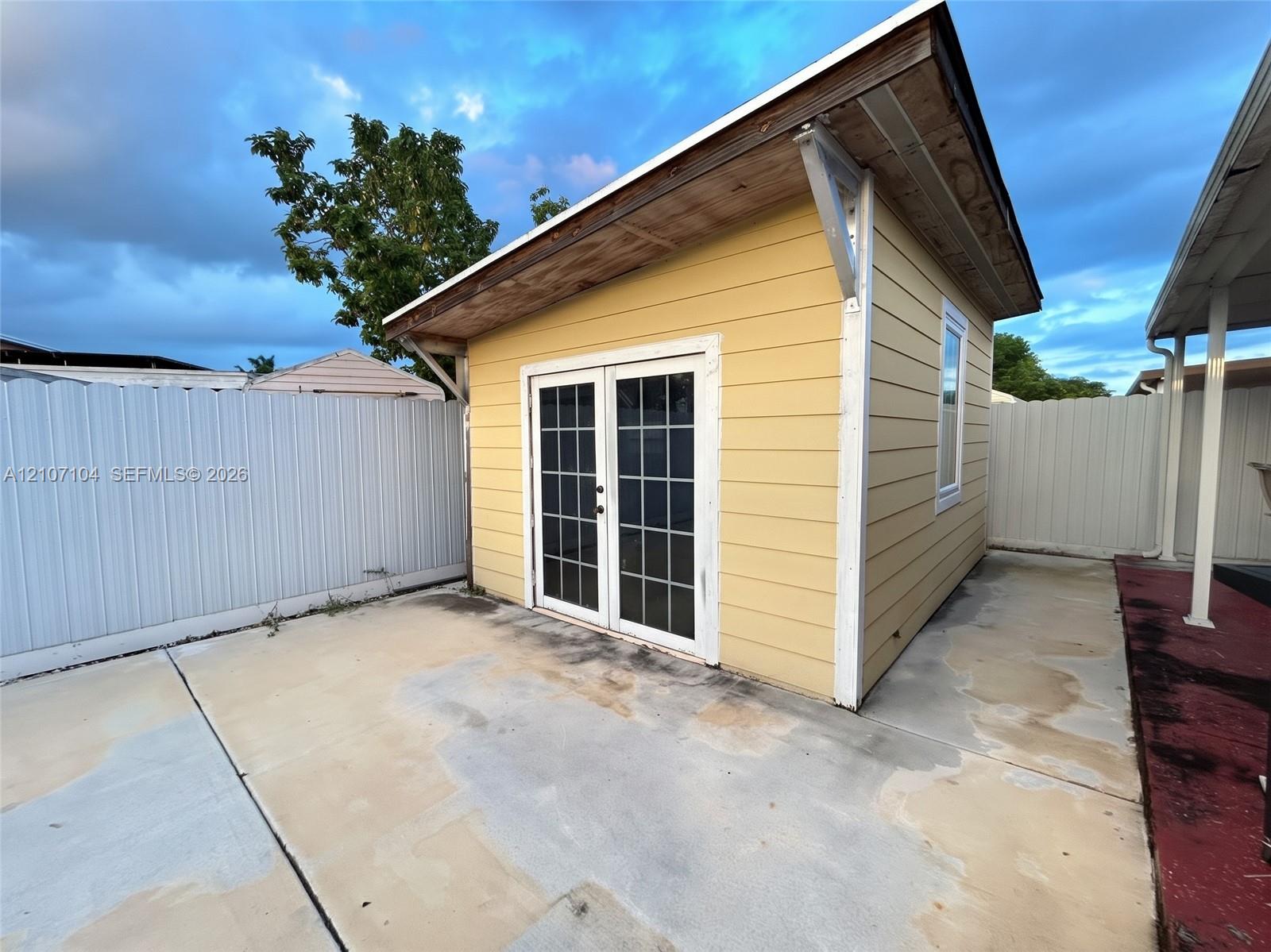 Detached structure featuring yellow horizontal lap siding, a single-slope roof, white-framed French doors with glass panes, and a concrete patio