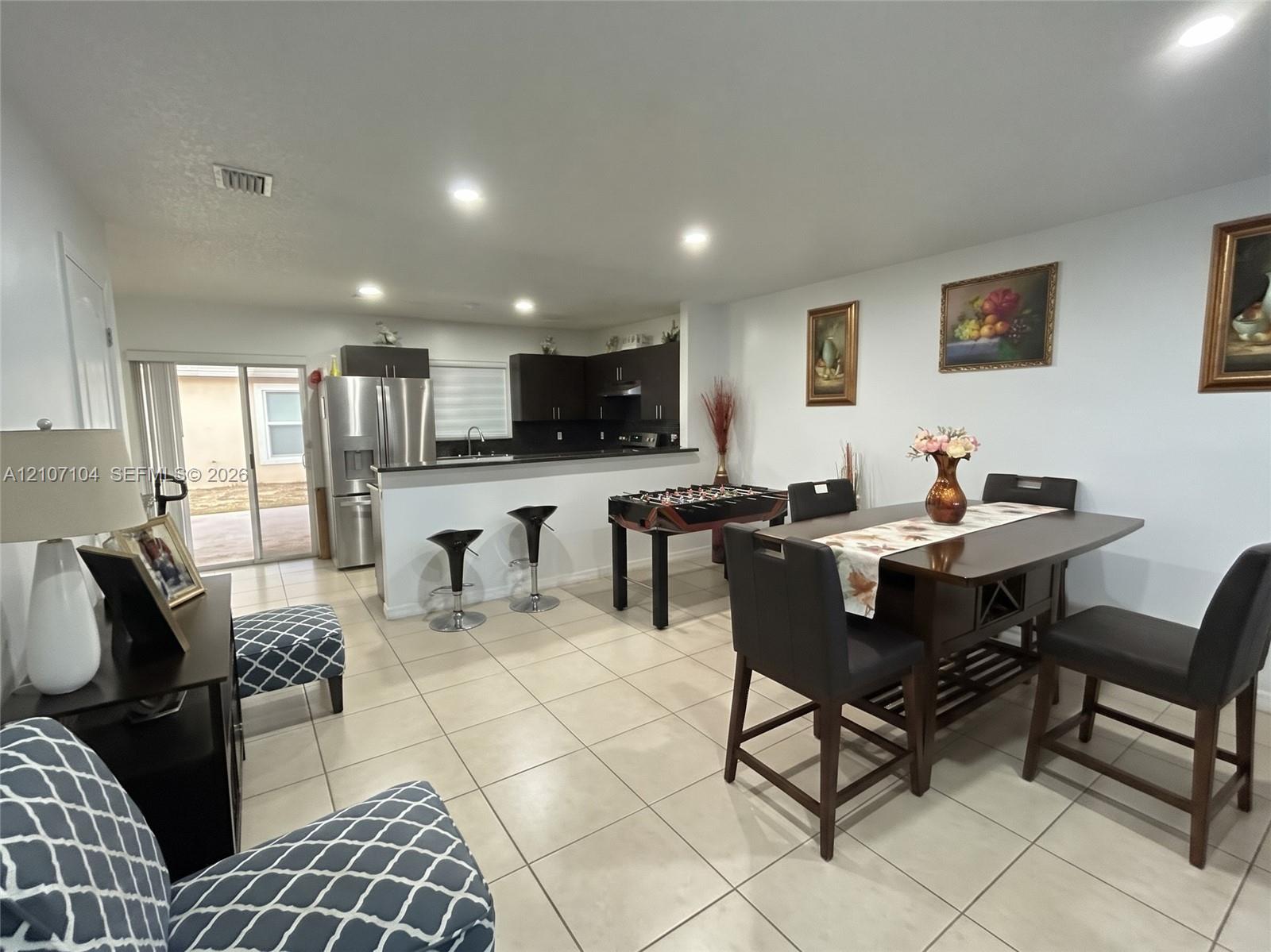 Open-concept area featuring ceramic tile flooring, recessed lighting, and a kitchen with dark cabinetry, stone-surface countertops, and a breakfast bar