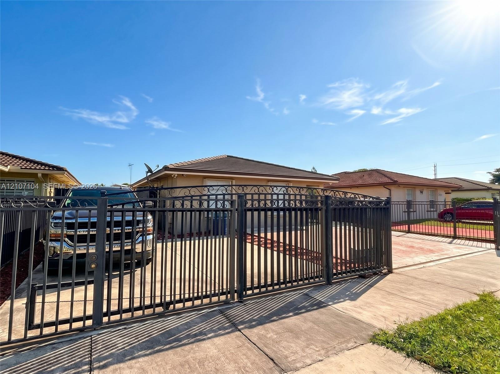 Single-story residence featuring a decorative metal perimeter fence with an arched gate, paved driveway, and low-slope roof