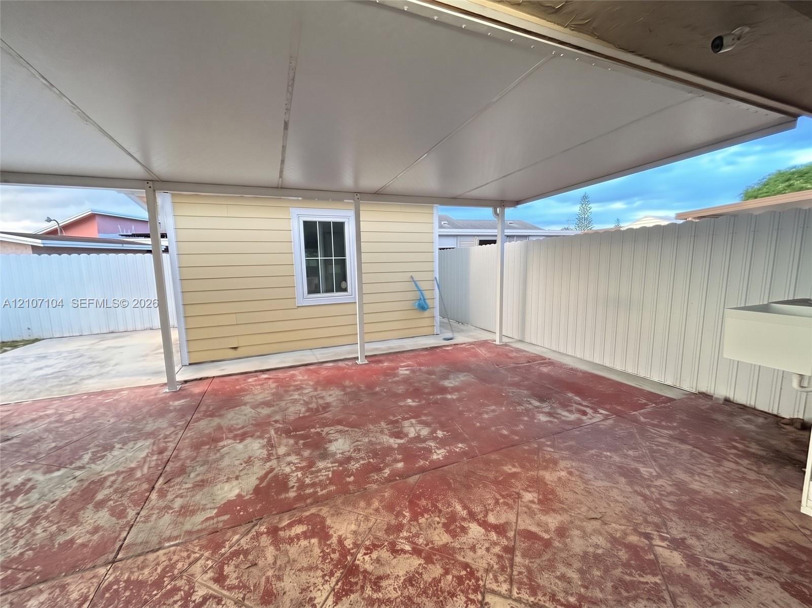 Covered outdoor patio featuring a concrete floor, horizontal siding, a multi-pane window, and a white privacy fence