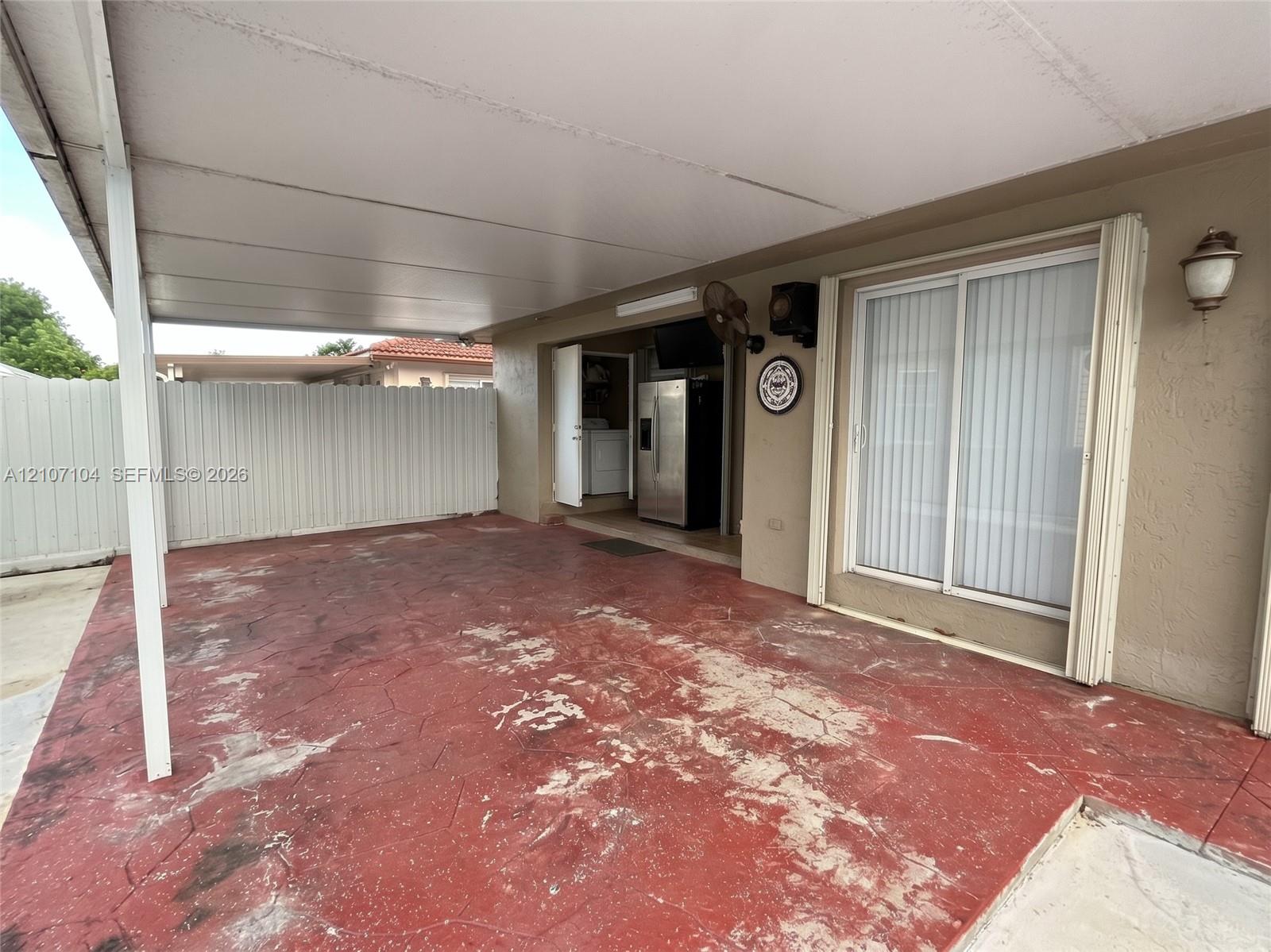 Covered patio featuring a stained concrete floor, sliding glass doors, and white vinyl perimeter fencing