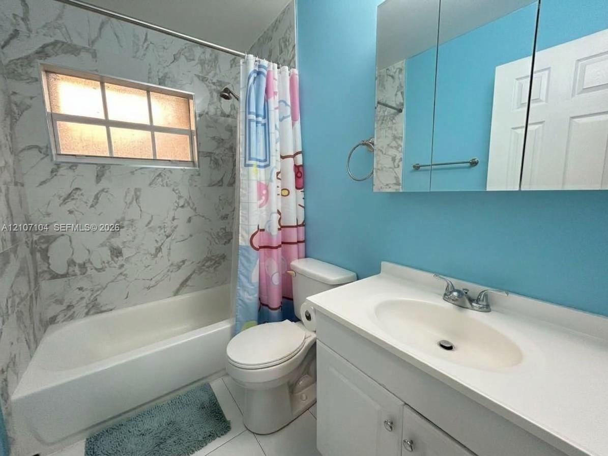 Bathroom featuring a tub-and-shower combination with patterned wall tile surround, a built-in recessed medicine cabinet, a single-basin vanity with solid-surface countertop, and an integrated horizontal window
