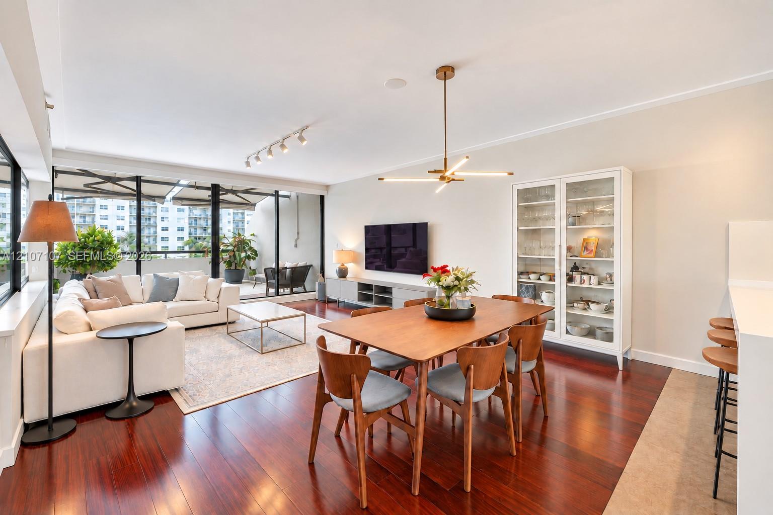 Open living and dining area featuring polished wood-finish flooring, floor-to-ceiling black-framed glass windows, integrated track lighting, and a modern multi-arm chandelier