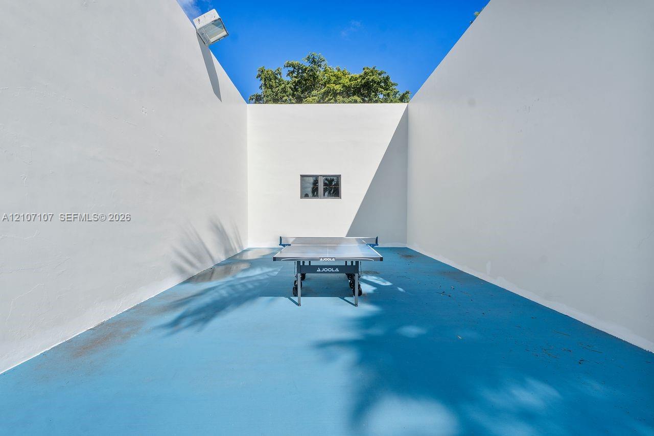 Enclosed outdoor recreation space featuring high perimeter masonry walls, painted blue concrete flooring, and an integrated exterior light fixture