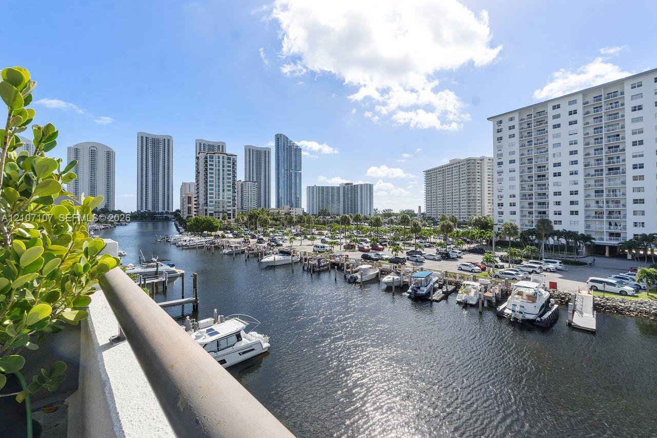 Balcony featuring a metal railing and panoramic water frontage overlooking a marina with docked watercraft and surrounding high-rise structures