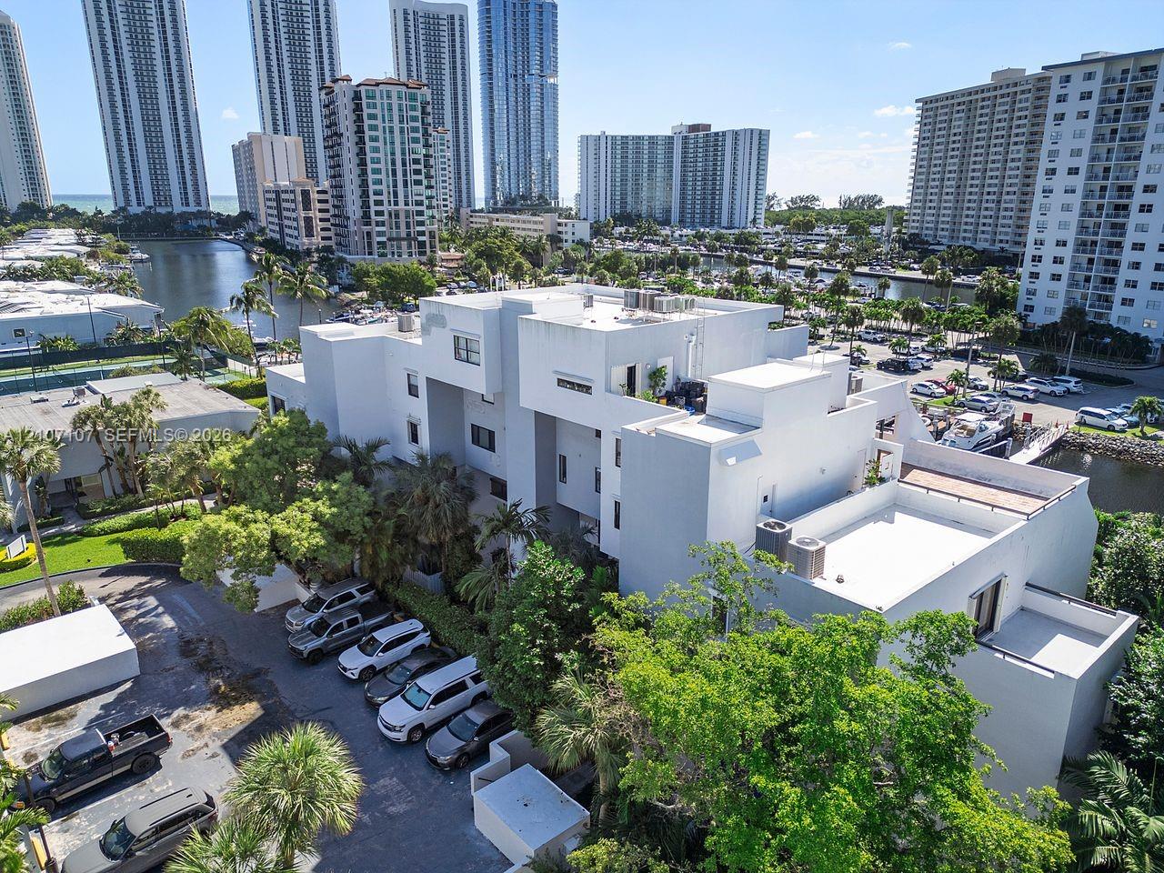 Multi-story structure featuring a smooth stucco exterior, flat roofline, integrated rooftop terrace, and surface parking area