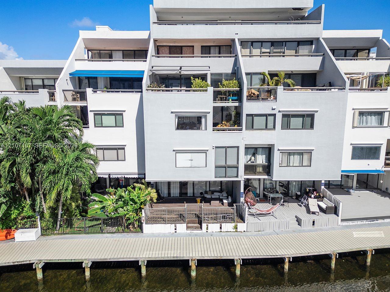 Multi-level contemporary exterior with tiered private balconies and ground-floor waterfront deck, featuring expansive glass sliding doors and a private deep-water dock