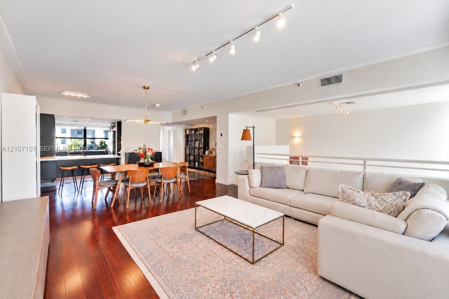 Open-concept living space featuring wood-finish flooring, recessed track lighting, a metallic chandelier, and a built-in kitchen island with cabinetry