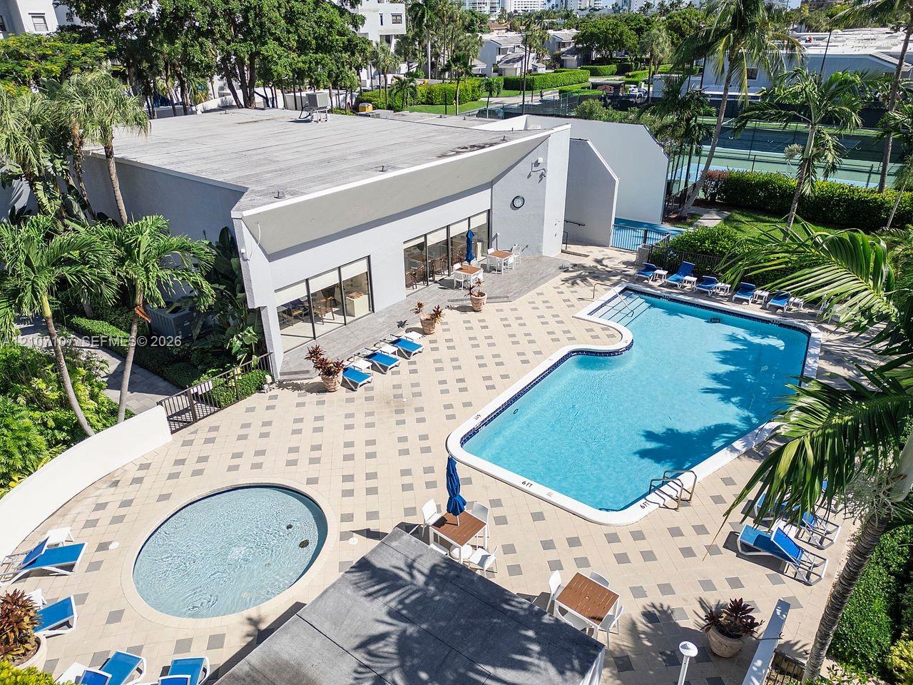 Community recreational area featuring a swimming pool, circular spa, paved pool deck, and tennis courts