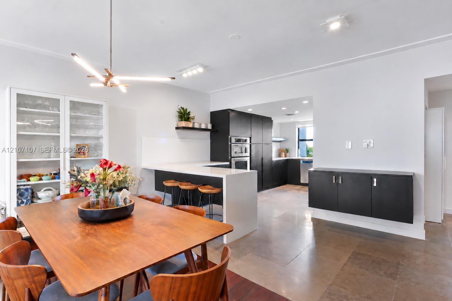 Modern kitchen featuring flat-panel cabinetry, waterfall-edge stone countertop, built-in double wall oven, contemporary multi-arm pendant lighting, and stone-finish flooring
