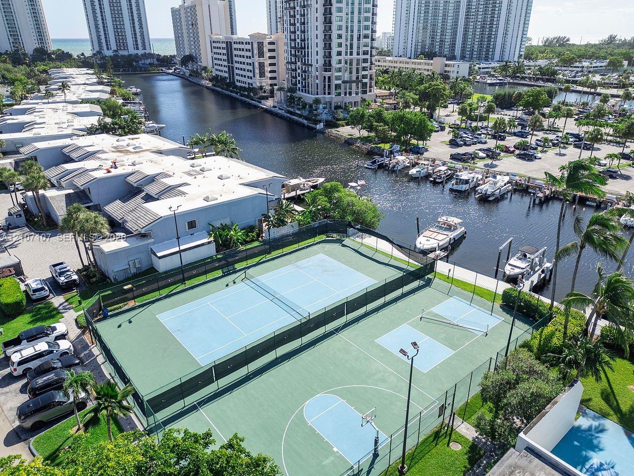 Recreational complex featuring multi-sport courts for tennis, pickleball, and basketball, enclosed by perimeter fencing and illuminated by overhead lighting
