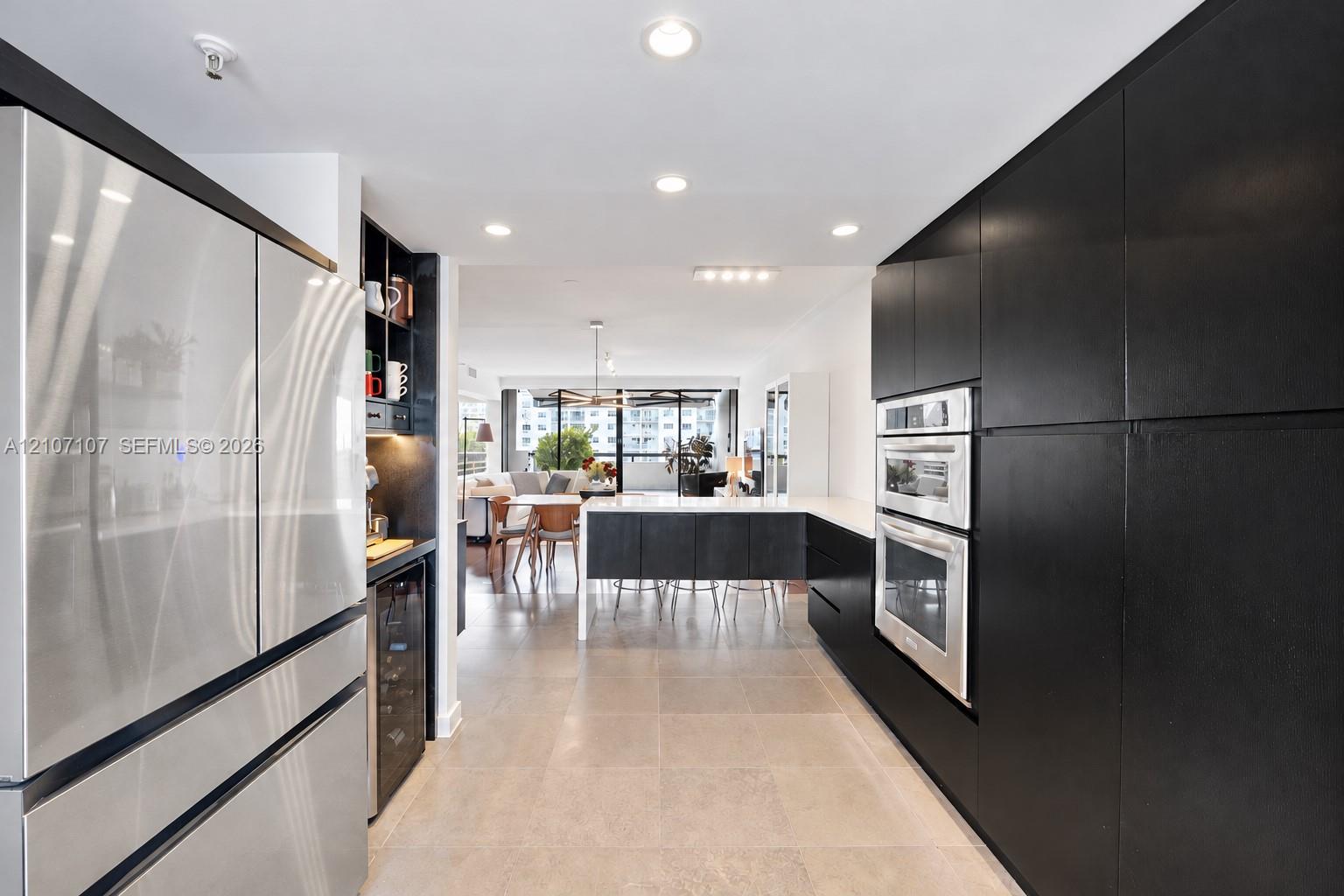 Modern kitchen featuring matte black flat-panel cabinetry, stainless steel double wall ovens, built-in beverage refrigerator, large stone-surface peninsula, and recessed lighting
