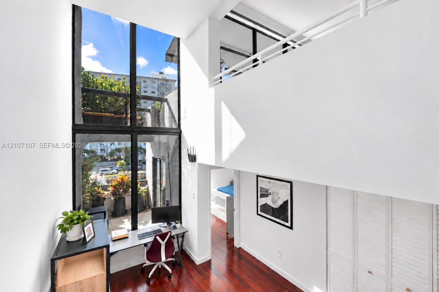 Double-height interior featuring floor-to-ceiling windows, white railings, wood-finish flooring, and built-in closet cabinetry