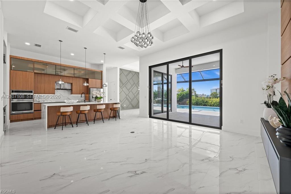 Coffered ceilings with recessed lighting, large-format tile flooring, wood-finish cabinetry, built-in stainless steel double ovens, and multi-panel sliding glass doors Coffered ceilings with recessed lighting, large-format tile flooring, wood-finish cabinetry, built-in stainless steel double ovens, and multi-panel sliding glass doors