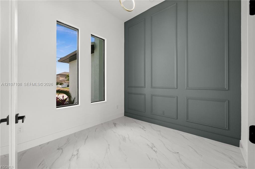 Interior space featuring large-format tile flooring with a neutral veining pattern, charcoal-toned wall with wainscoting molding, dual tall windows, and matte black hardware