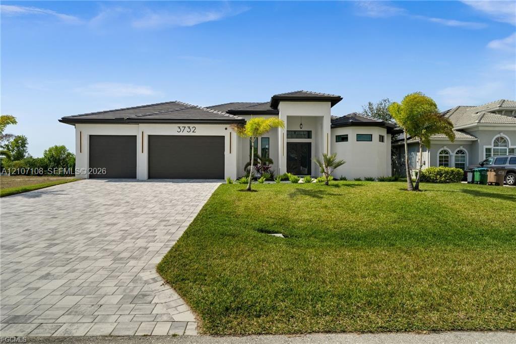 Contemporary stucco exterior featuring a flat tile roof, paver driveway, covered entryway, and three-car garage