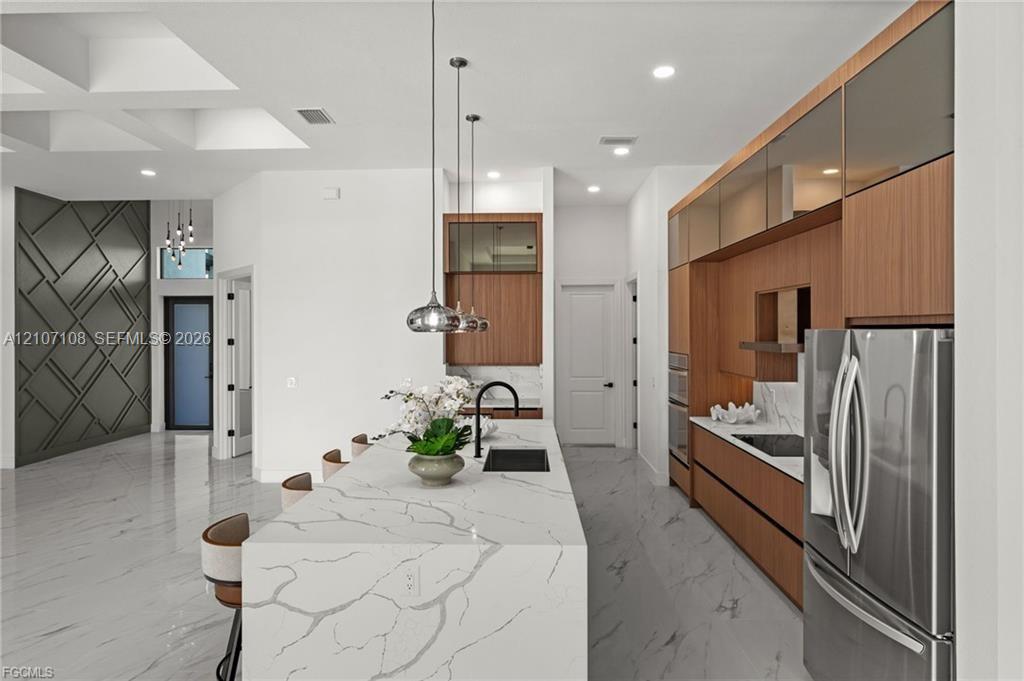 Kitchen featuring stone-patterned countertops, wood-finish cabinetry, recessed lighting, drop-pendant fixtures, and large-format tile flooring