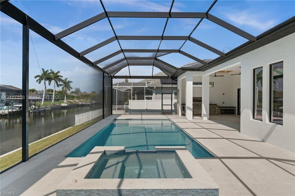 Screened lanai featuring an in-ground swimming pool, elevated spa, built-in outdoor kitchen, and canal-front location