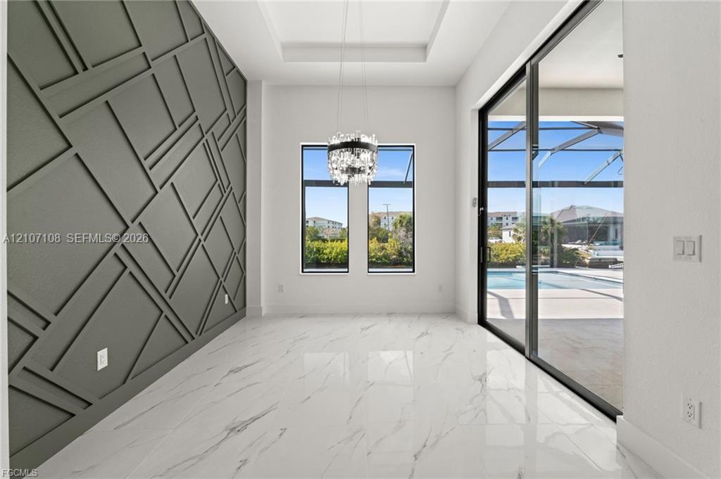 Geometric millwork accent wall, high-gloss stone-finish flooring, tray ceiling with crystal-style chandelier, and floor-to-ceiling sliding glass doors Geometric millwork accent wall, high-gloss stone-finish flooring, tray ceiling with crystal-style chandelier, and floor-to-ceiling sliding glass doors