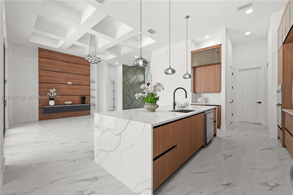 Kitchen featuring an expansive island with waterfall-edge stone countertop, wood-finish cabinetry, coffered ceiling, stone-finish flooring, and statement pendant lighting Kitchen featuring an expansive island with waterfall-edge stone countertop, wood-finish cabinetry, coffered ceiling, stone-finish flooring, and statement pendant lighting