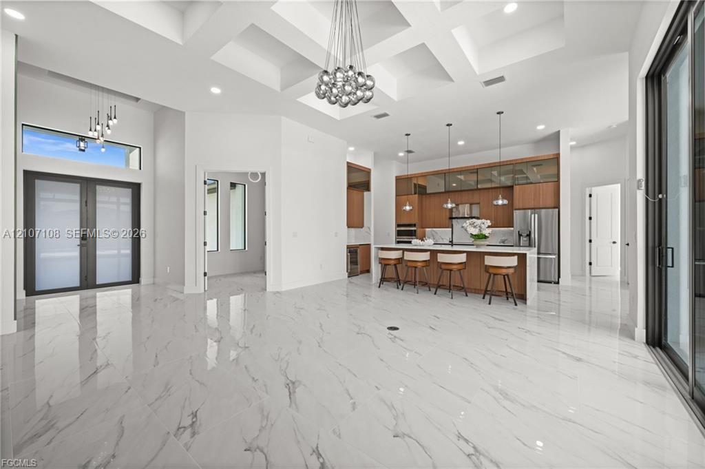 Coffered ceilings featuring recessed lighting, polished stone-finish flooring, custom cabinetry with integrated stainless steel appliances, large kitchen island with quartz countertops, and floor-to-ceiling glass sliding doors Coffered ceilings featuring recessed lighting, polished stone-finish flooring, custom cabinetry with integrated stainless steel appliances, large kitchen island with quartz countertops, and floor-to-ceiling glass sliding doors