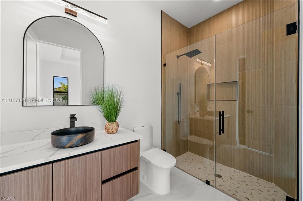 Floating vanity with a stone-finish countertop, arched wall mirror, vessel sink with matte black hardware, and a walk-in shower featuring tile walls, a built-in recessed niche, and a glass enclosure