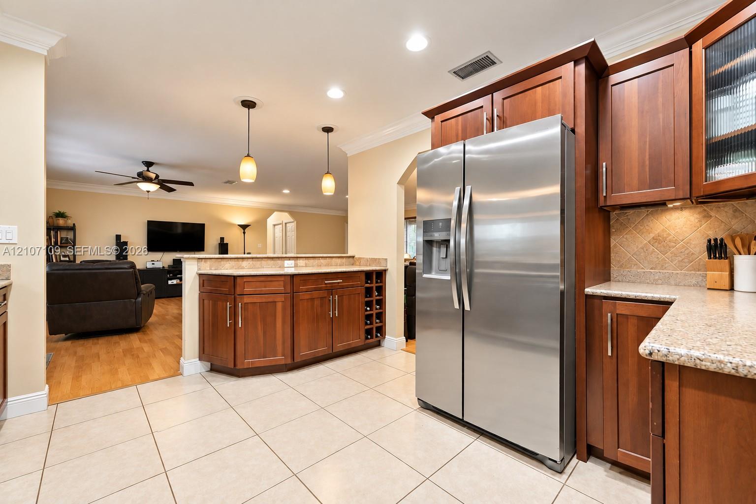 Kitchen featuring wood cabinetry, stone countertops, stainless steel refrigerator, built-in wine rack, and pendant lighting