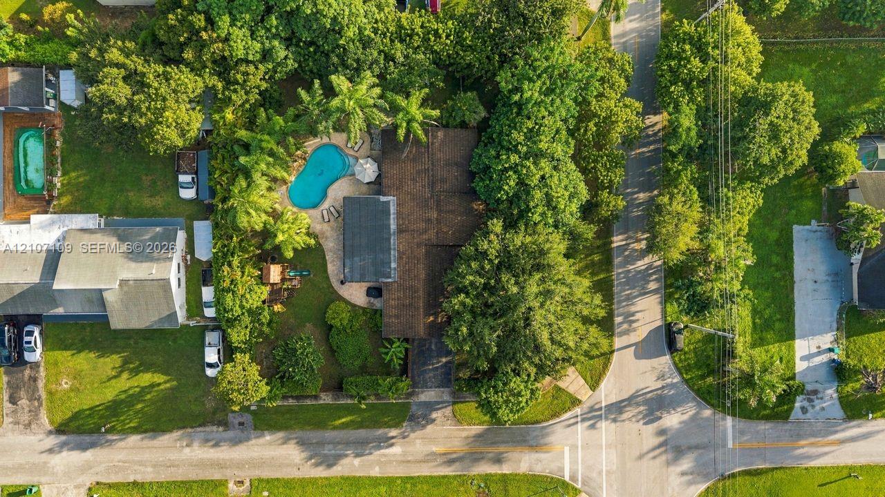 Aerial perspective featuring an expansive lot with a swimming pool, paved patio, mature trees, and a multi-section asphalt shingle roof