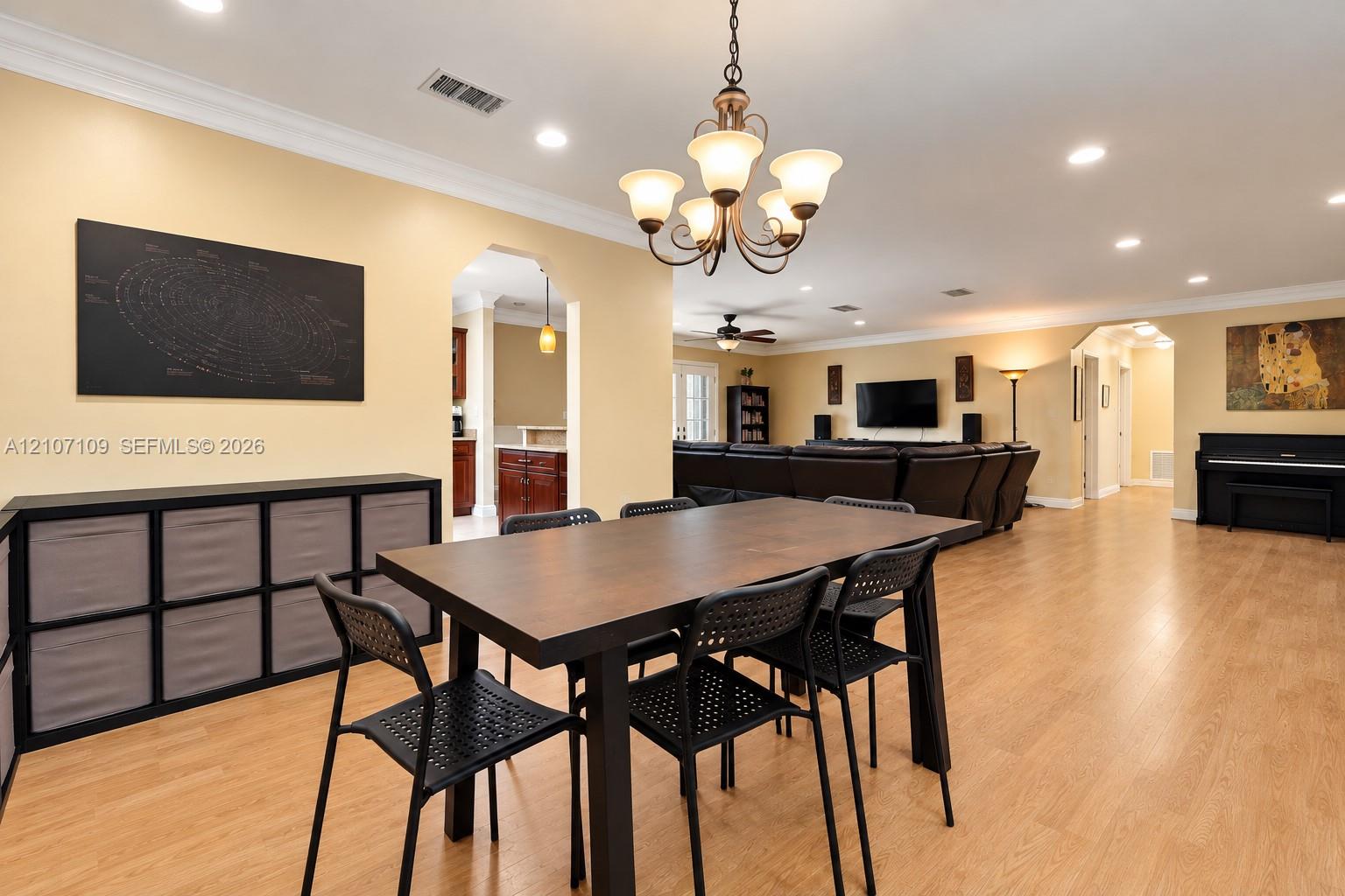 Open-concept floor plan featuring wood-finish flooring, crown molding, recessed lighting, and a multi-arm chandelier